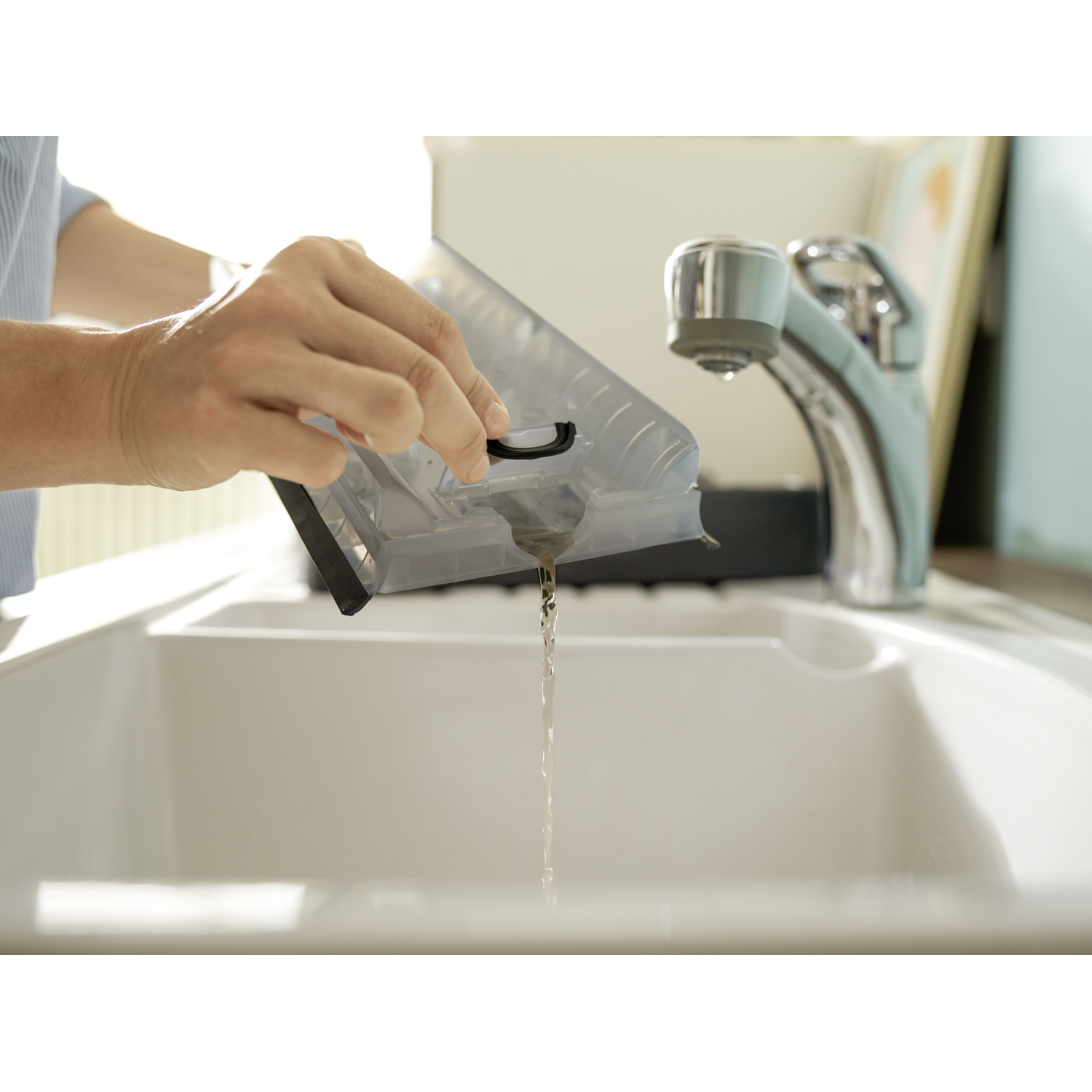 Hand pouring water from a vacuum cleaner container into a white sink.