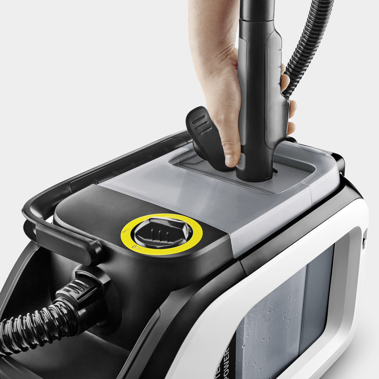 Un nettoyeur vapeur. Une main place un accessoire de nettoyage sur le dessus. Noir et blanc avec un cadran jaune.