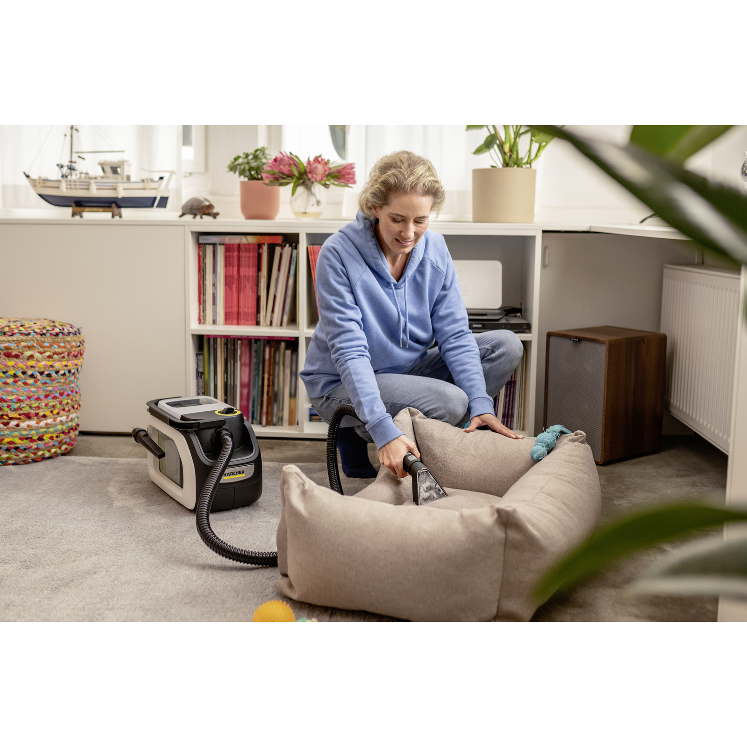 Femme passant l'aspirateur sur un lit pour chien avec un petit aspirateur.