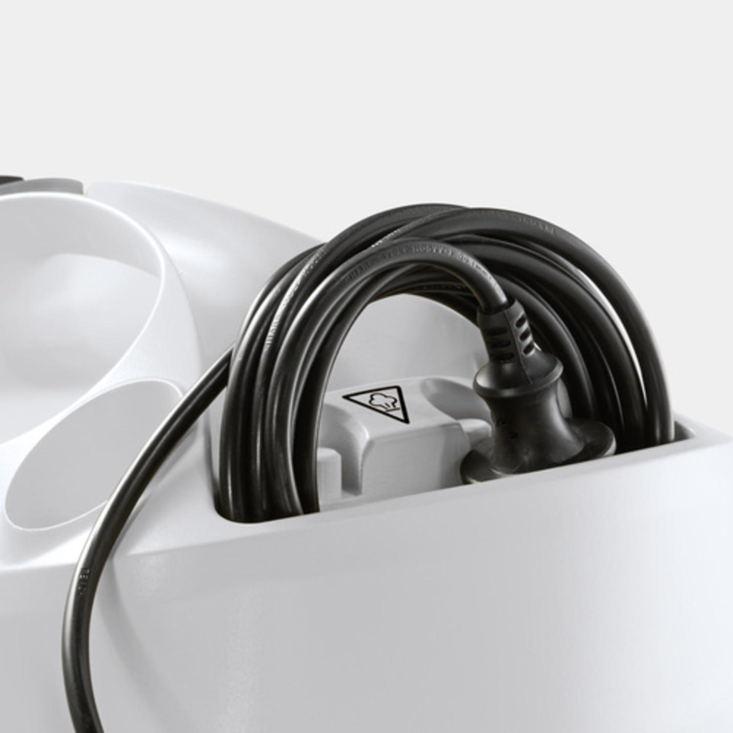 A white appliance with a coiled black power cord plugged in and a safety symbol.