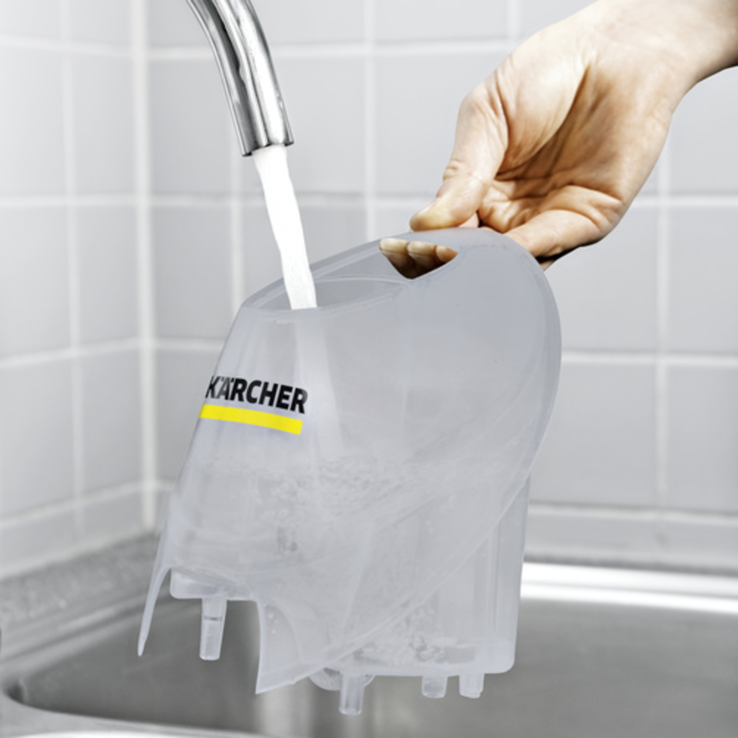 A hand pours water into a Karcher cleaning device, held over a sink.