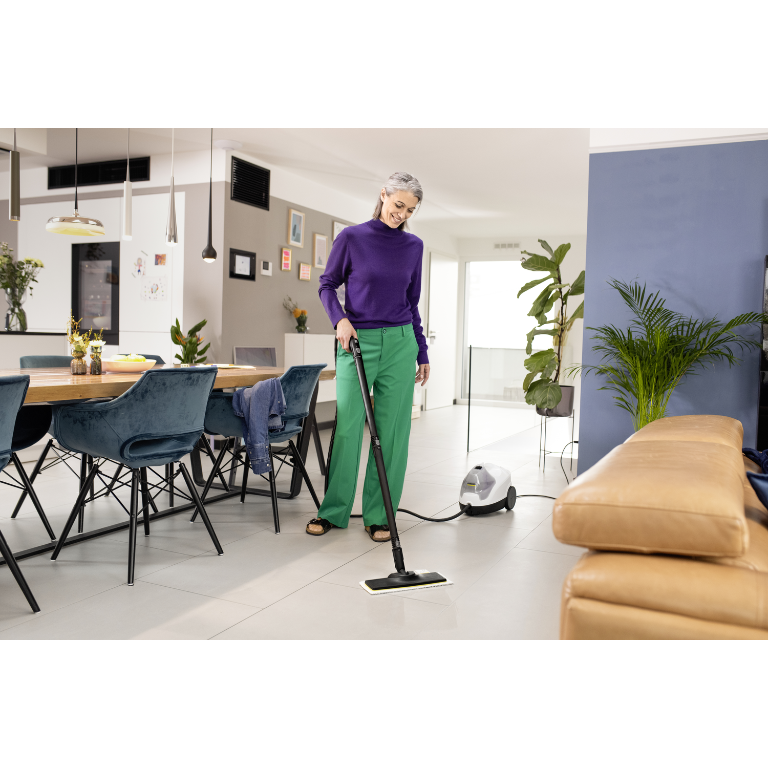 Woman in purple shirt and green pants, steaming a floor with white cleaner.