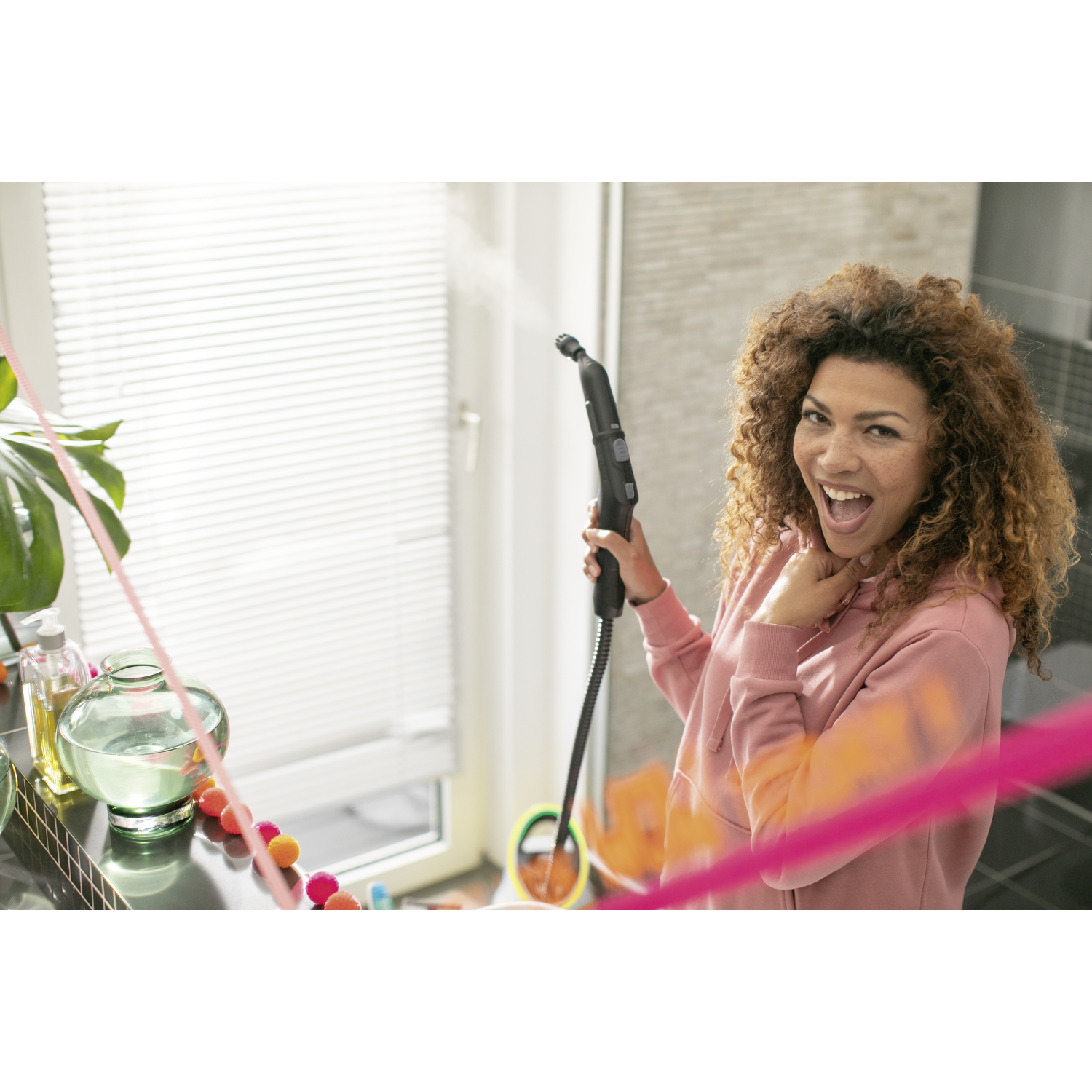 A woman smiling while holding a black steam cleaner, with colorful decorations on the left.