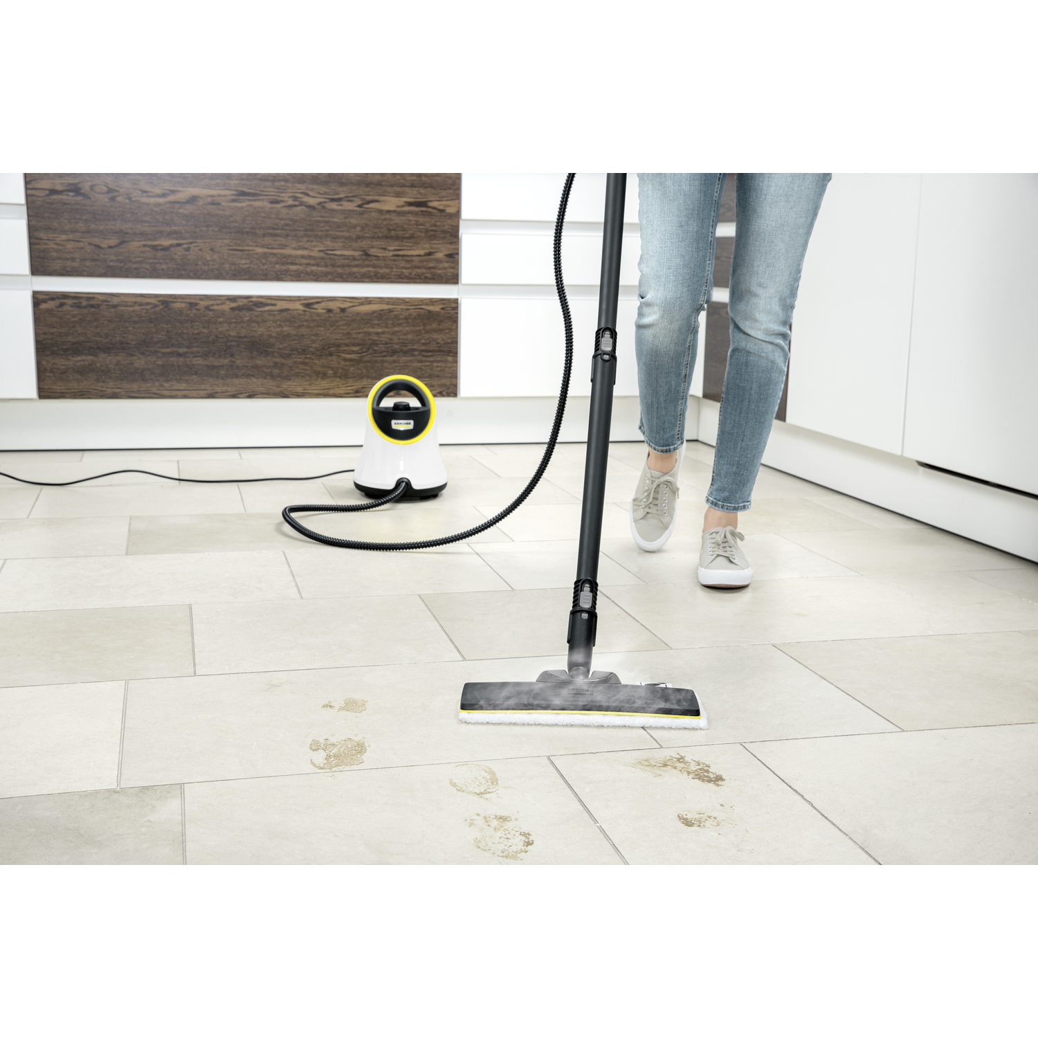A person steaming the floor with a white and yellow steam cleaner. The floor has footprints.