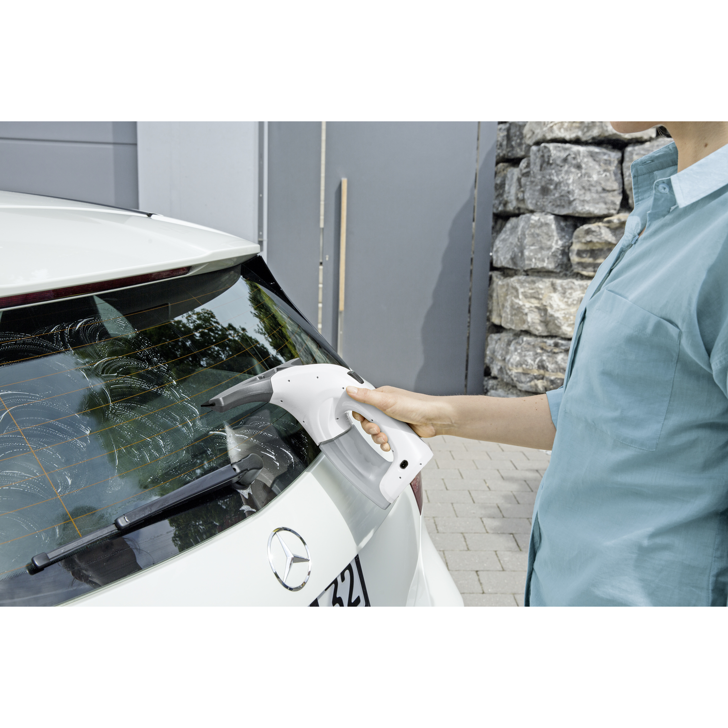 Une femme nettoyant une vitre de voiture avec un nettoyeur de vitres Kärcher blanc sur une voiture blanche.