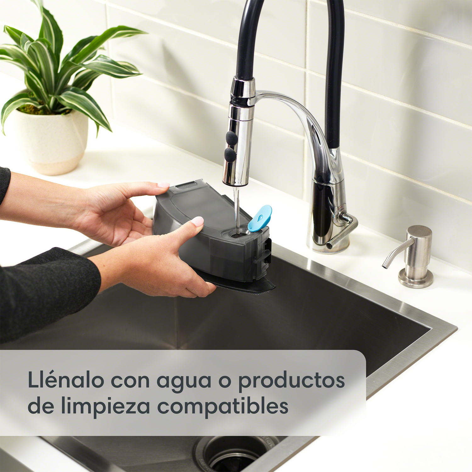 Manos llenando un recipiente oscuro con agua en un fregadero, productos de limpieza cerca.