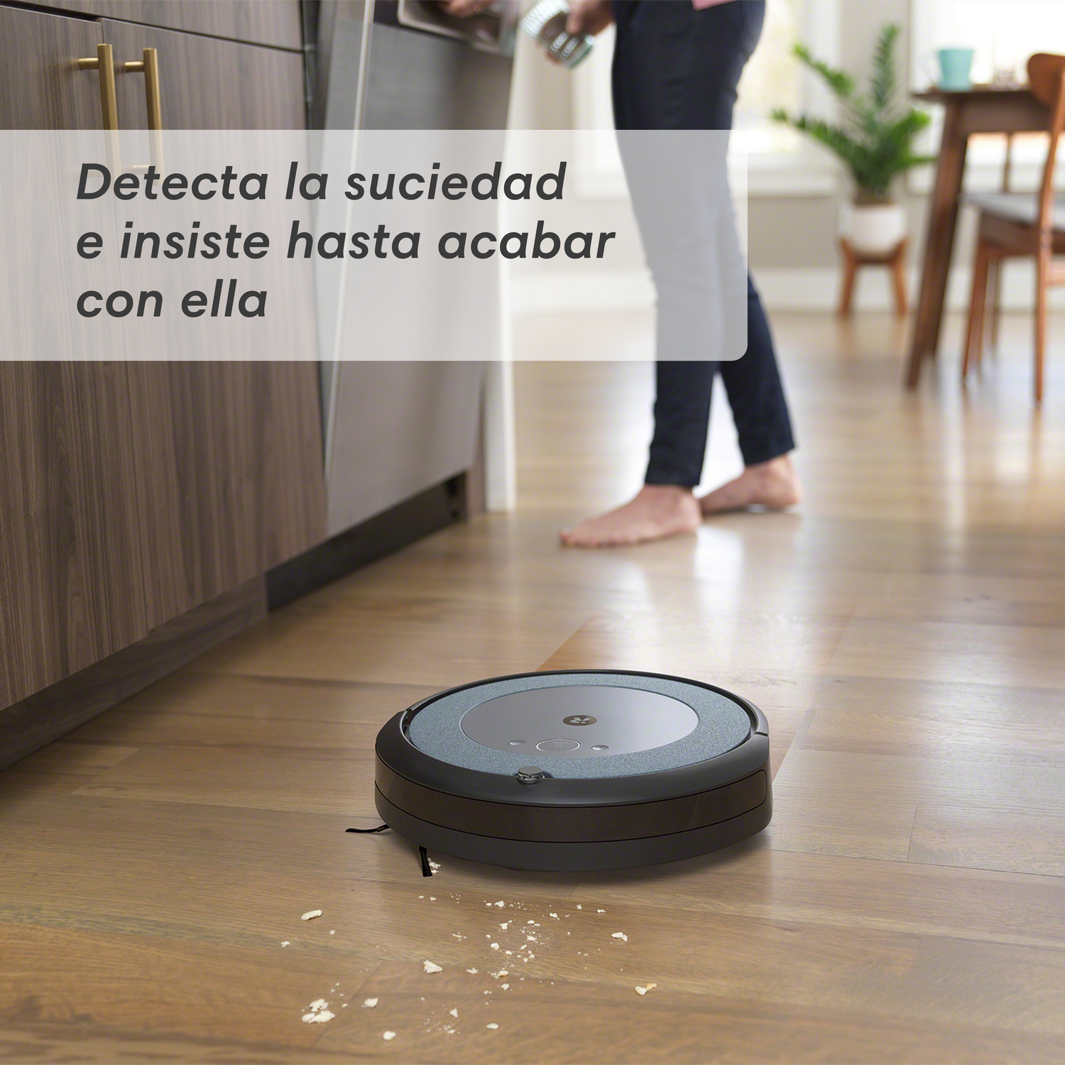 Robot aspirador en suelo de madera. Una persona en el fondo. Texto: Detecta la suciedad.