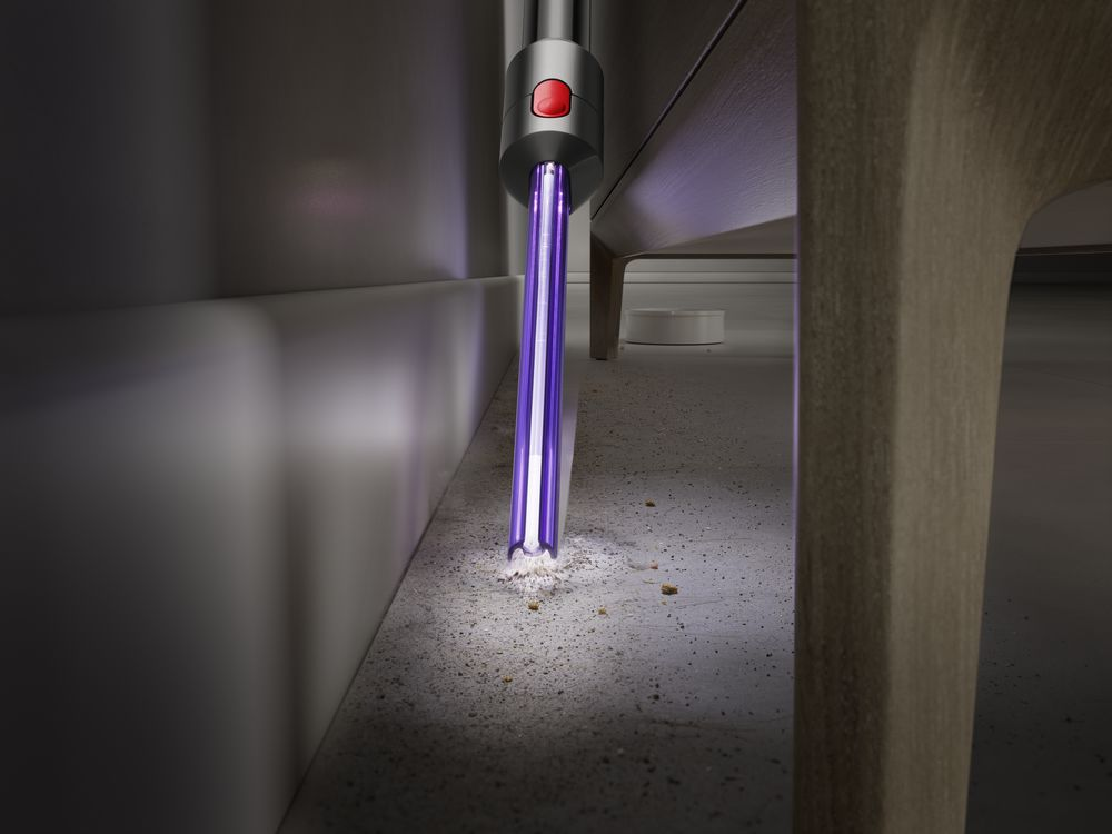 Una aspiradora con luz UV limpiando debajo de una mesa en un piso gris.
