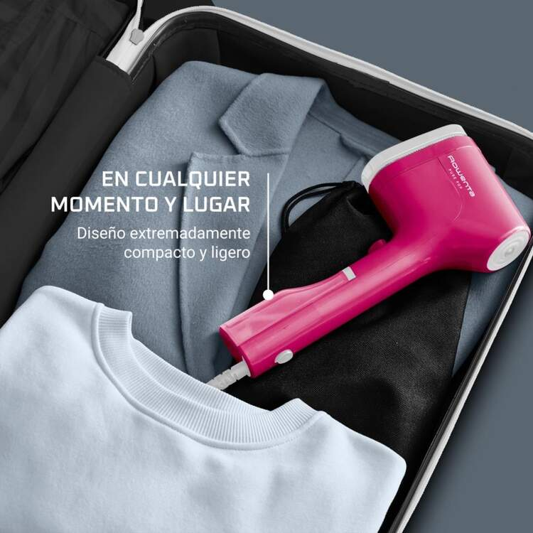 Un vaporizador de viaje rosa dentro de una maleta abierta con ropa, fondo blanco.