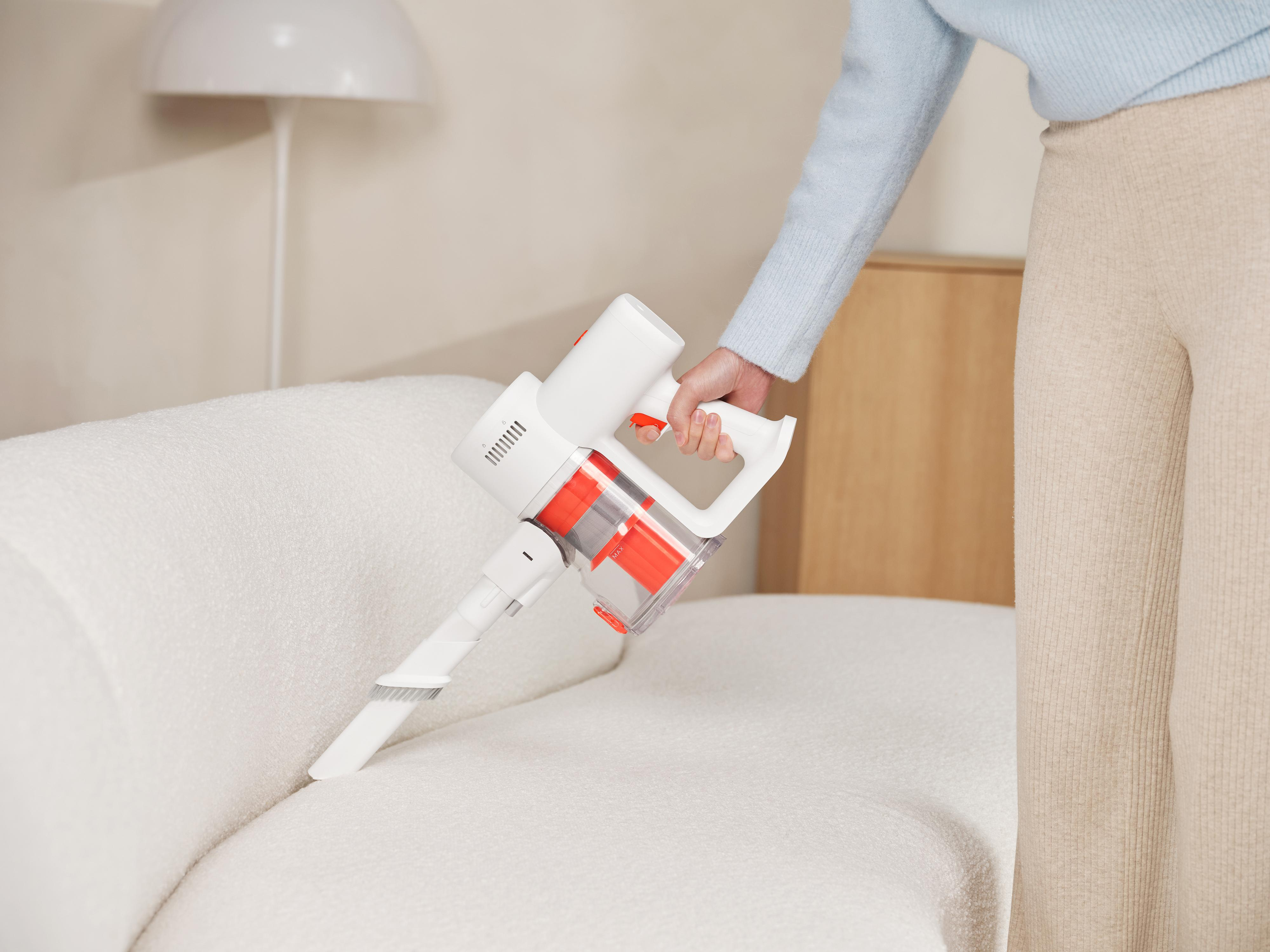 Osoba używająca białego i czerwonego odkurzacza ręcznego na białej sofie.
