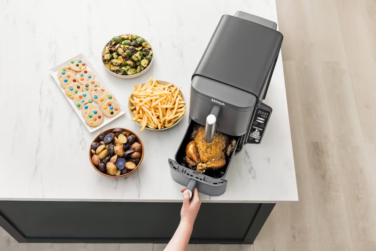 Freidora de aire en una encimera con alimentos, incluyendo galletas y pollo asado.
