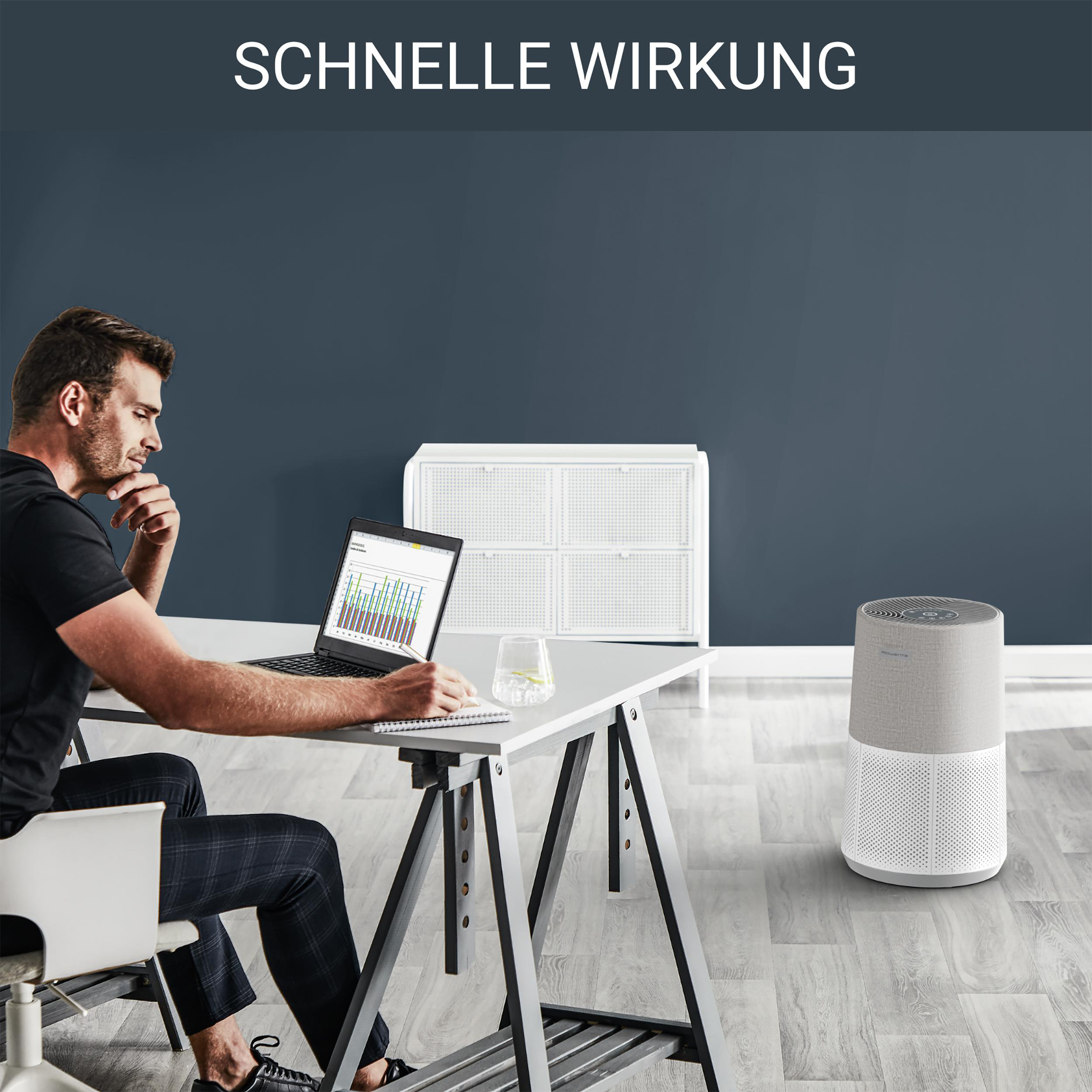 Mann arbeitet am Laptop neben Luftreiniger im Raum.