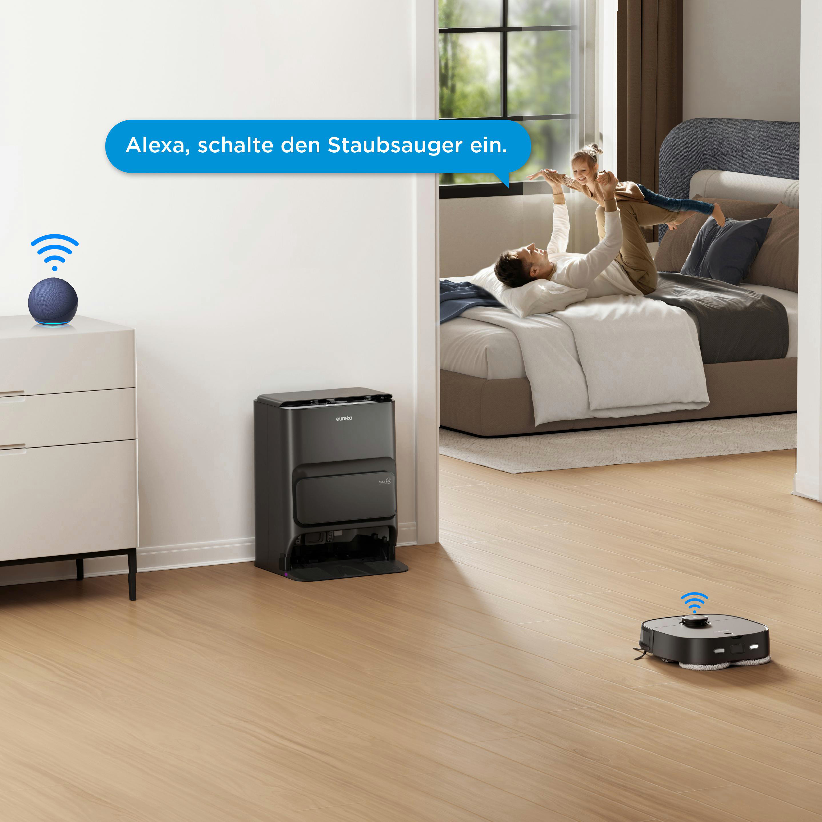 Familie in einem Raum mit einem Roboterstaubsauger und einem Alexa-Lautsprecher. Text: 'Alexa, schalte den Staubsauger ein'.