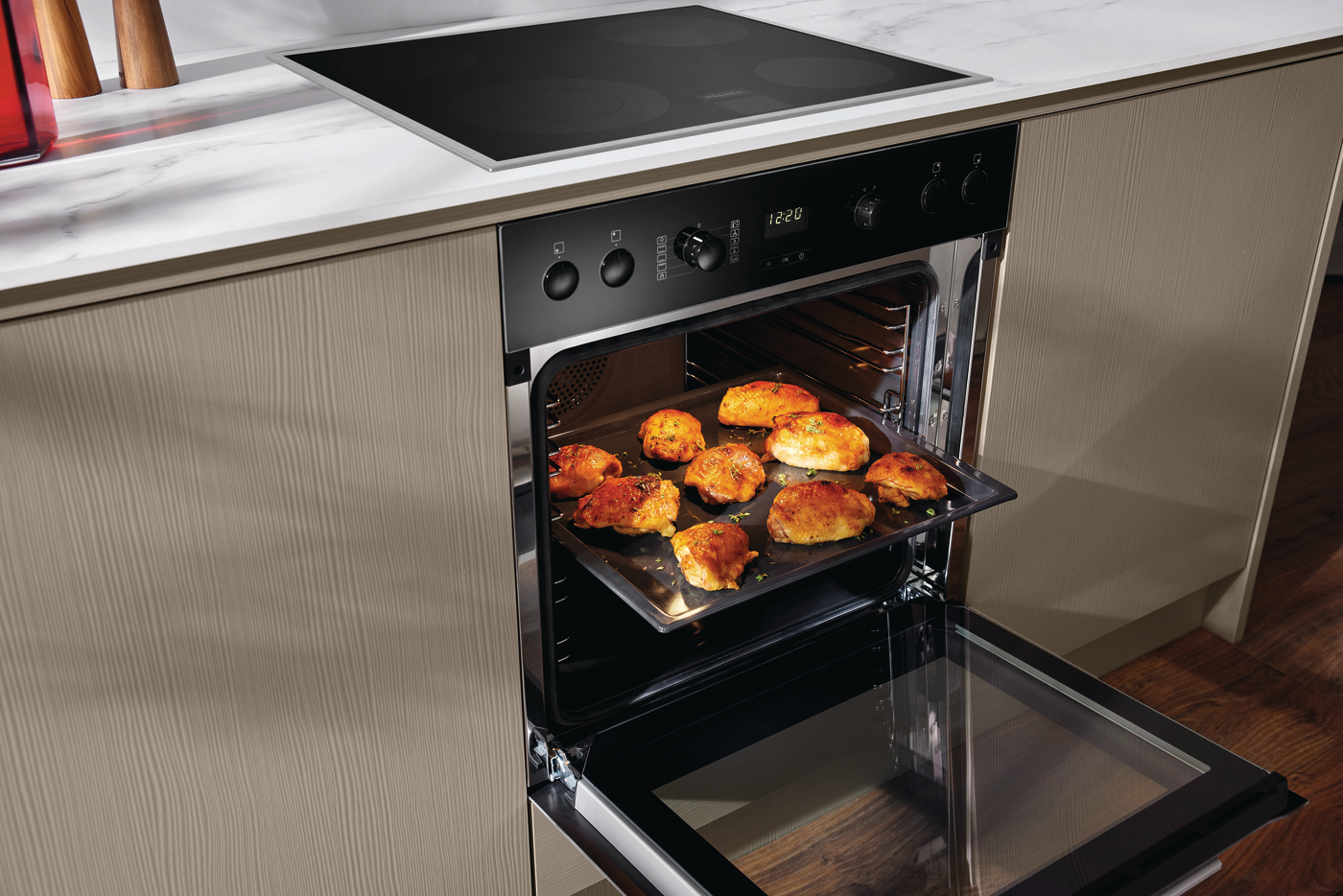 Ein Backofen mit Hähnchen auf einem Blech, offen, mit Kochfeld darüber.