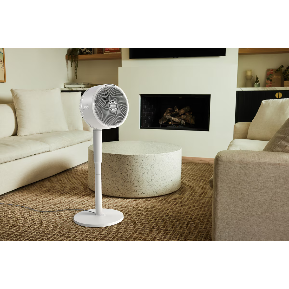 Ventilador de pie blanco en una sala de estar, cerca de una mesa redonda, un sofá y chimenea.