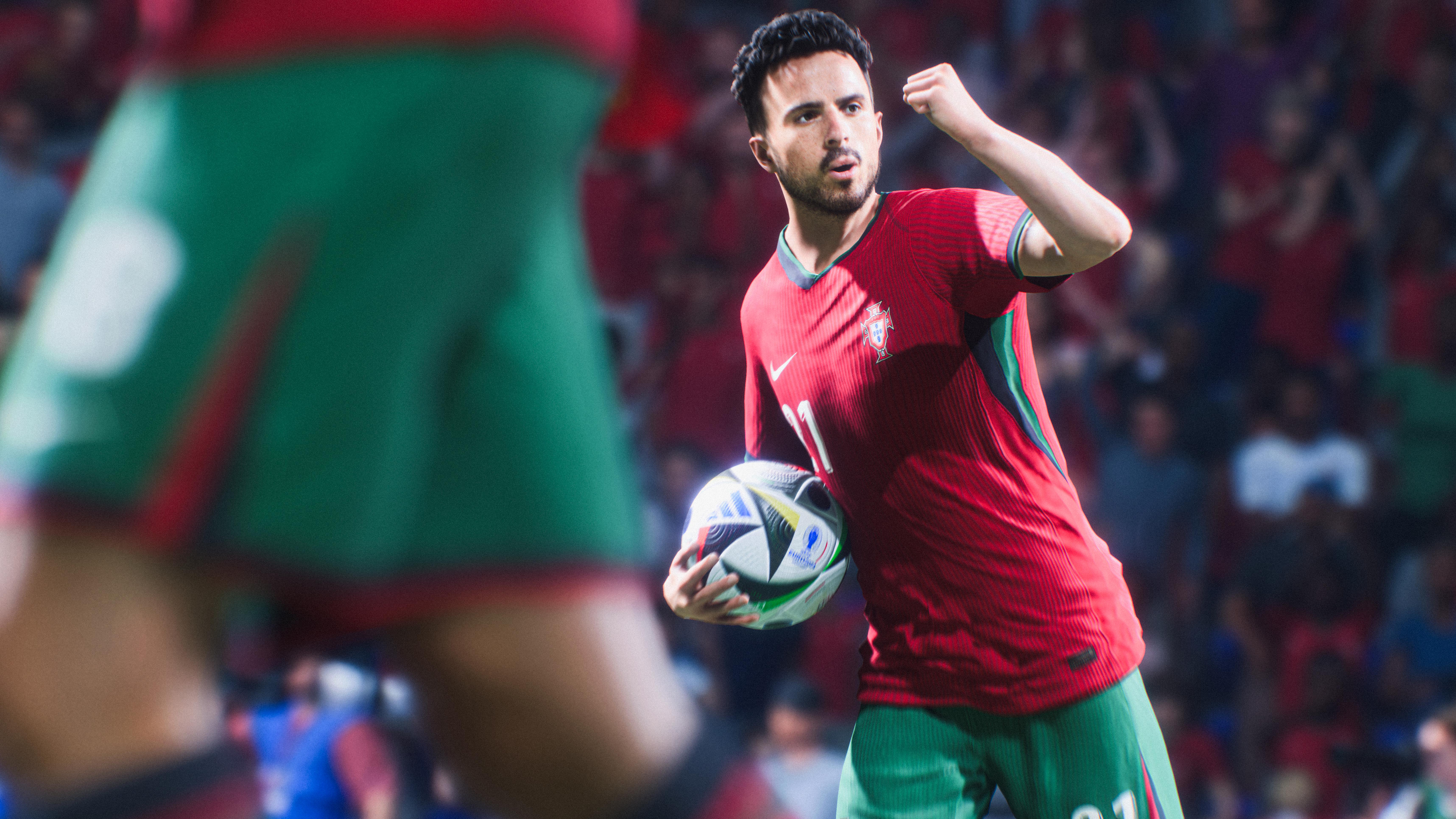 Ein Fußballspieler in einem roten Trikot hält einen Ball und jubelt mit erhobener Faust während eines Spiels.