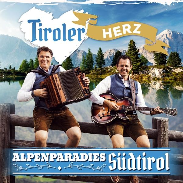 Zwei Männer in traditioneller bayerischer Kleidung spielen Musik an einem Bergsee.