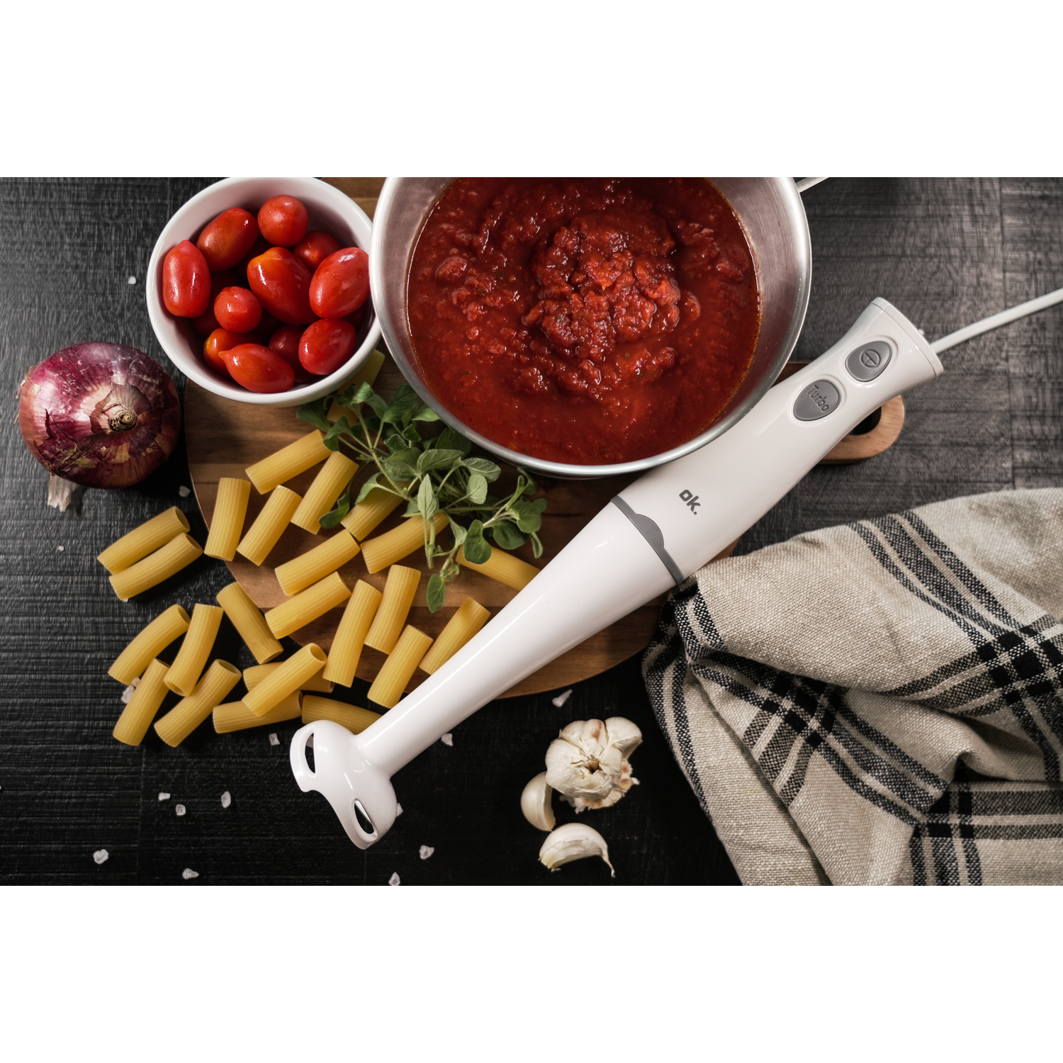 Immersion blender and ingredients: tomatoes, pasta, sauce, onion, garlic.