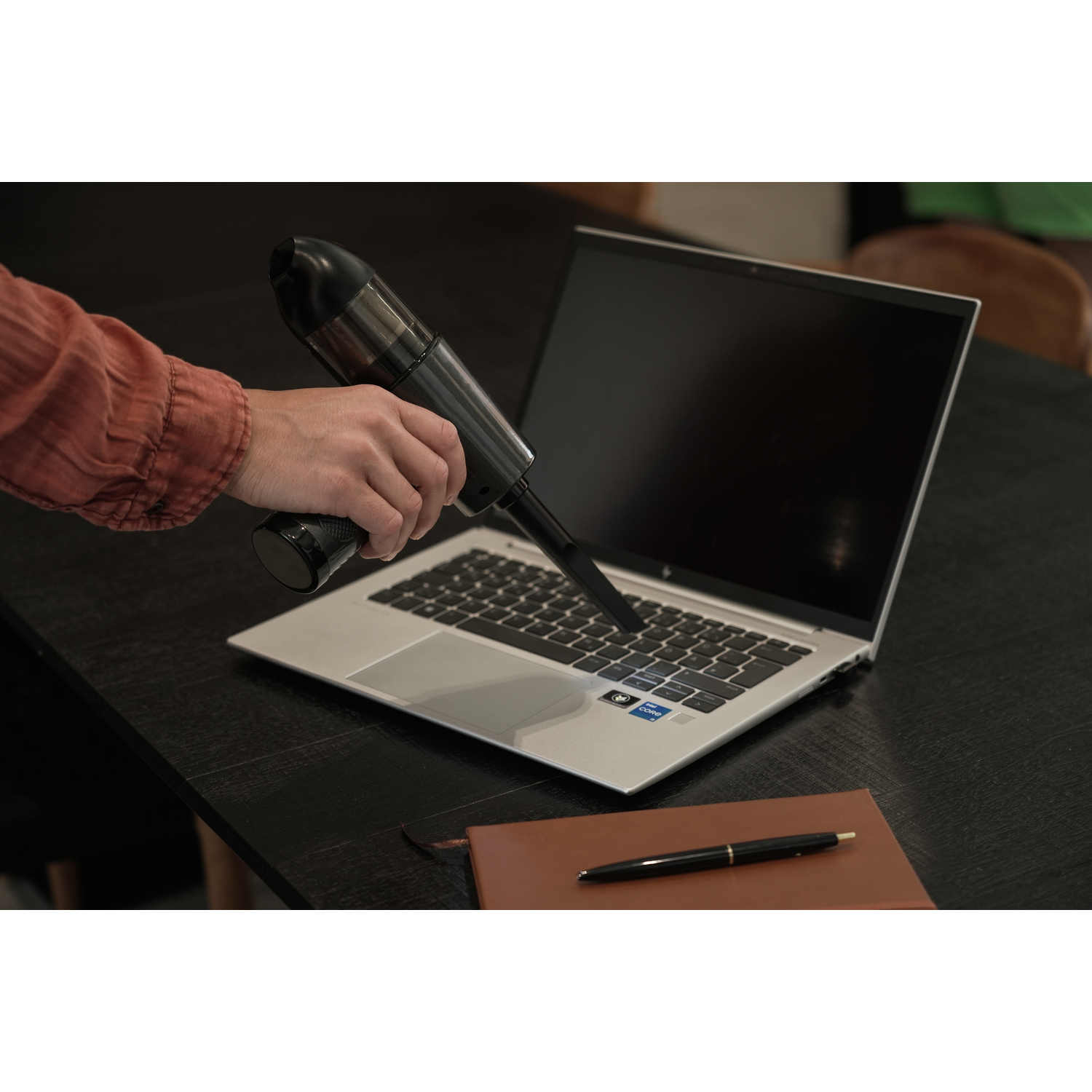 Person cleaning a laptop keyboard with a handheld vacuum cleaner.