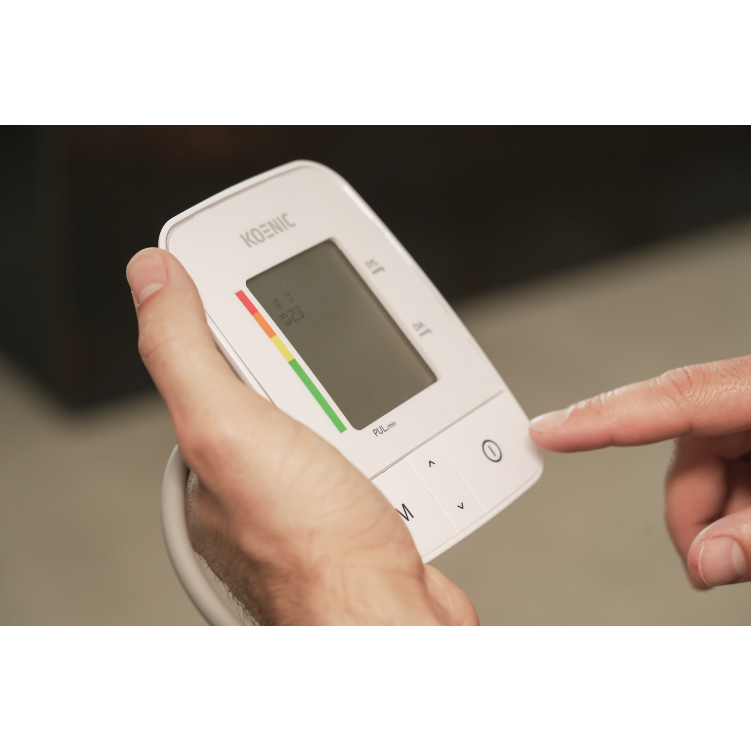 A person's hand holding a blood pressure monitor, pressing a button.