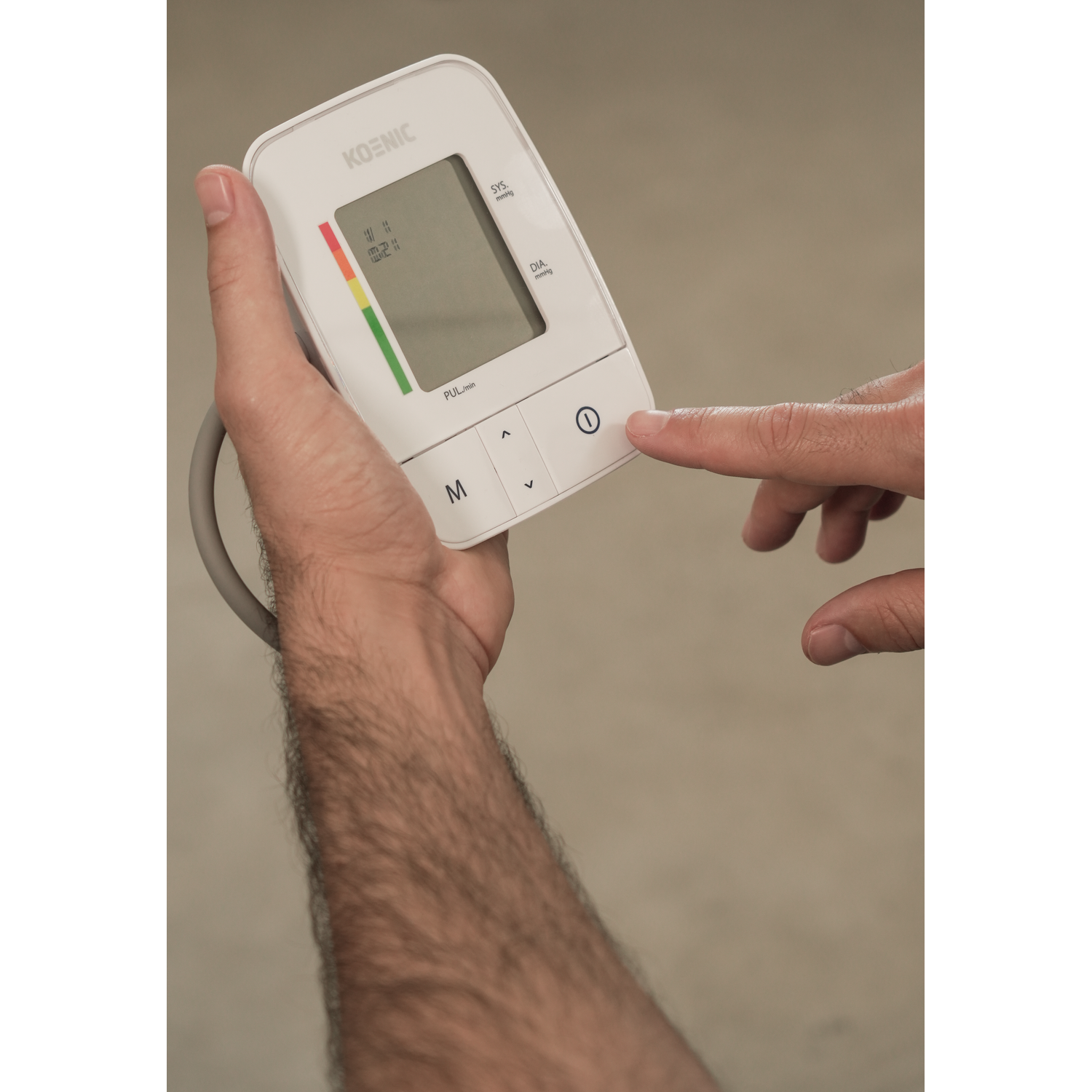 A person holds a blood pressure monitor and presses the power button with their finger.