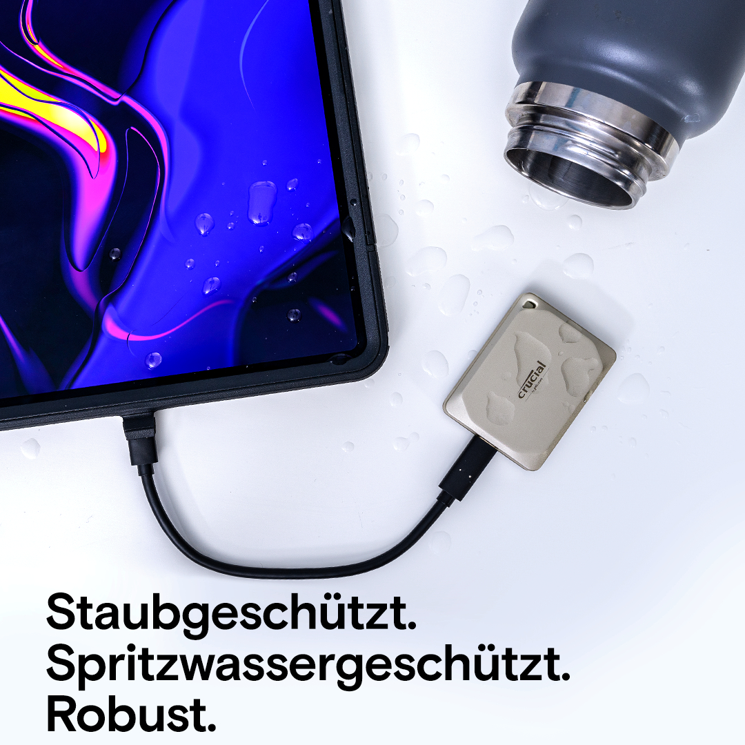 Tablet mit schwarzem Kabel, silbernem Datenspeicher und Wasserflasche auf weißer Oberfläche.