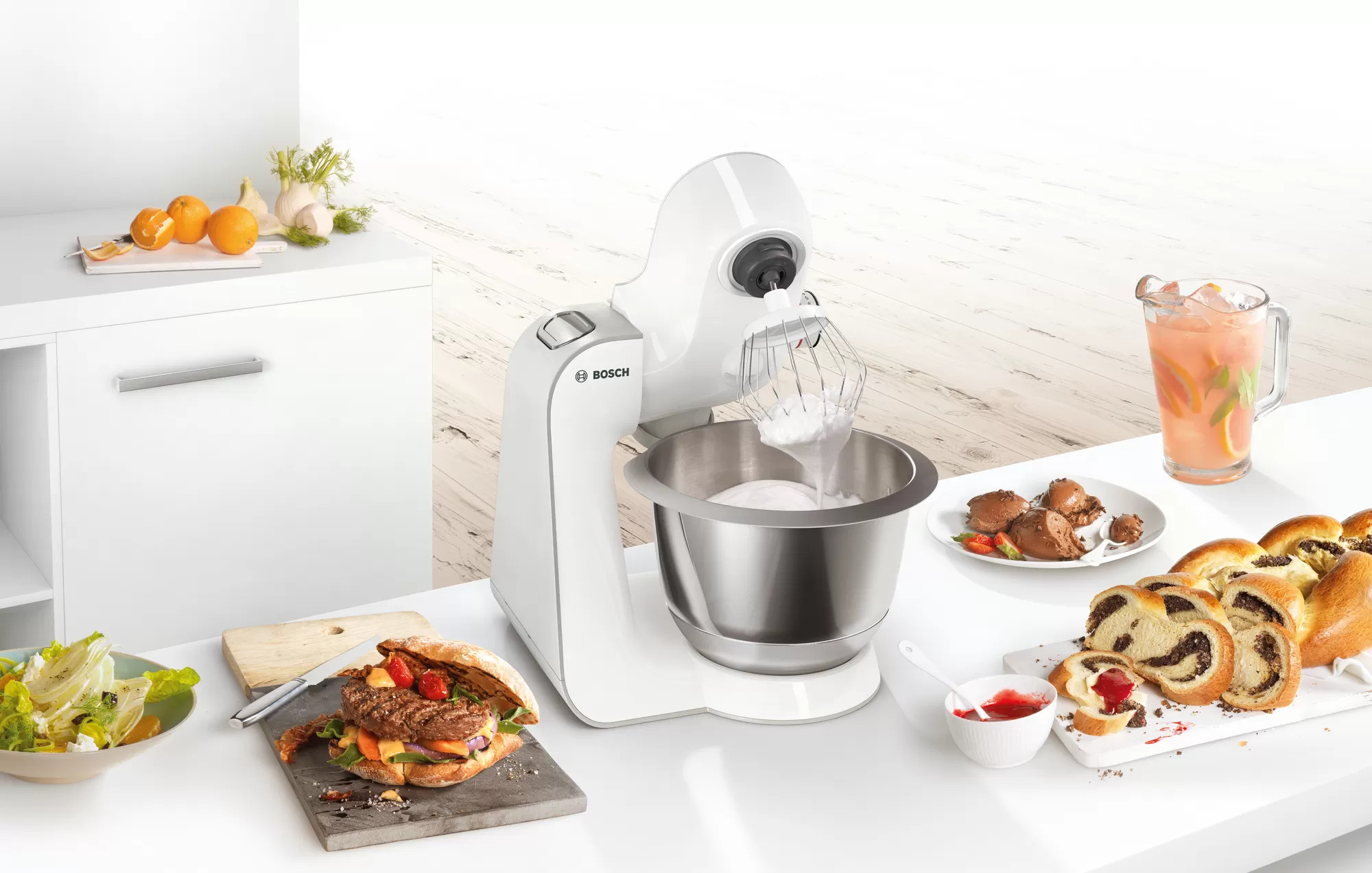 Biały mikser kuchenny z jedzeniem wokół, w tym burgerem i chlebem.