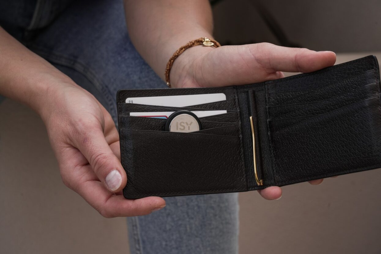 Mani che tengono un portafoglio aperto in pelle nera con carte e una moneta.