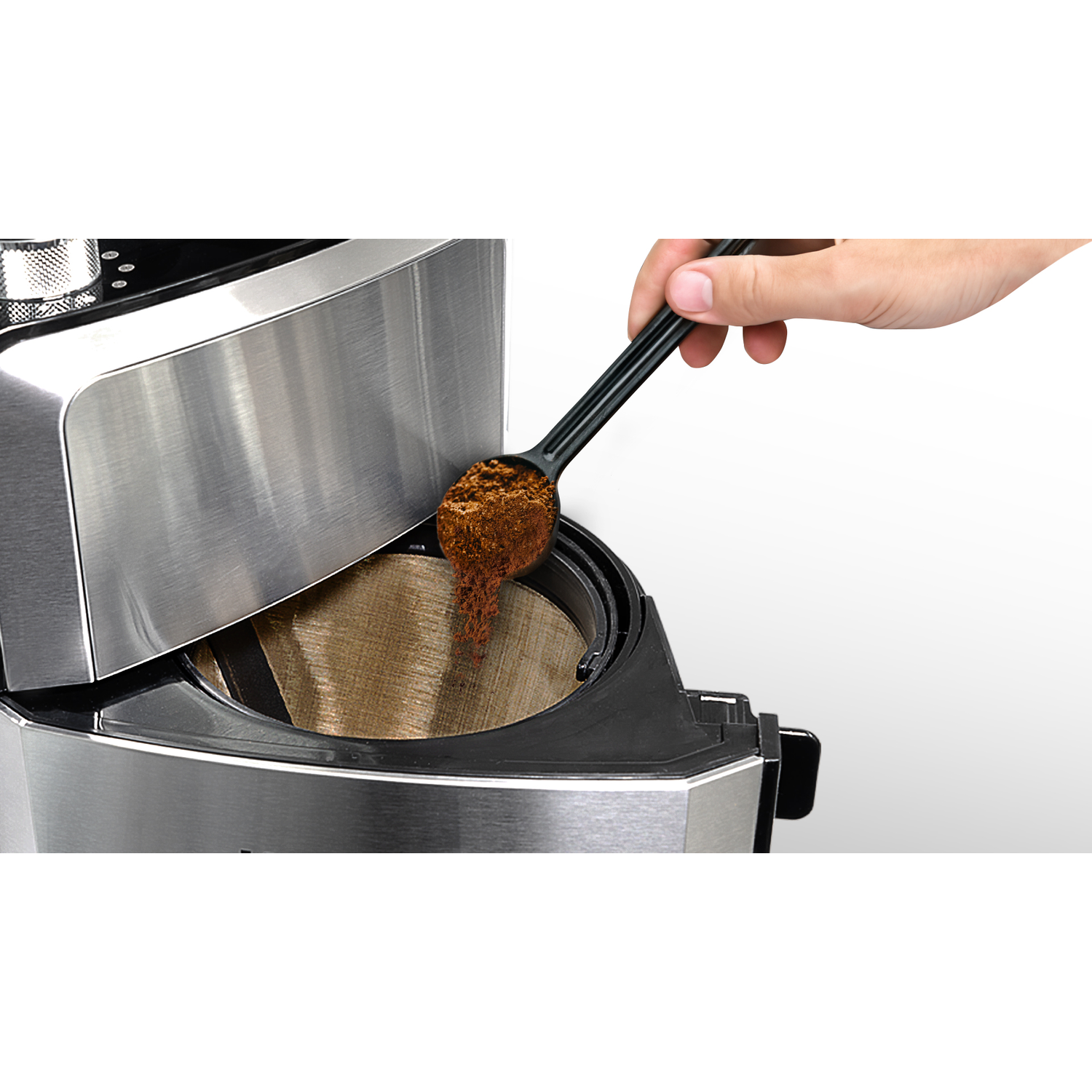 Coffee maker with coffee grounds being added to the filter. Spoon in action.