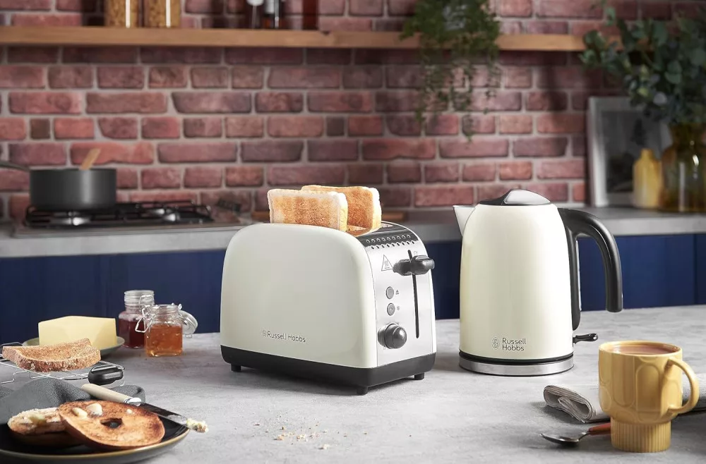 Scena di cucina con tostapane e bollitore. Toast nel tostapane. Burro, marmellata e bagel sul tavolo.