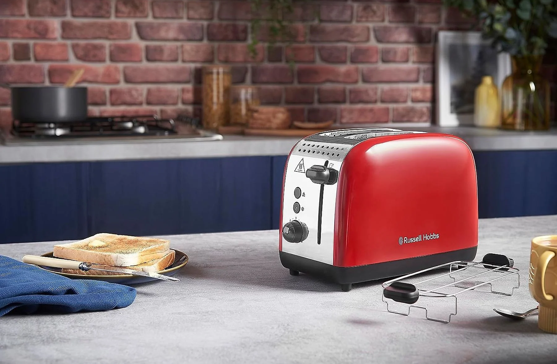 Tostapane rosso Russell Hobbs, toast ed elementi della cucina su un piano di lavoro grigio chiaro.