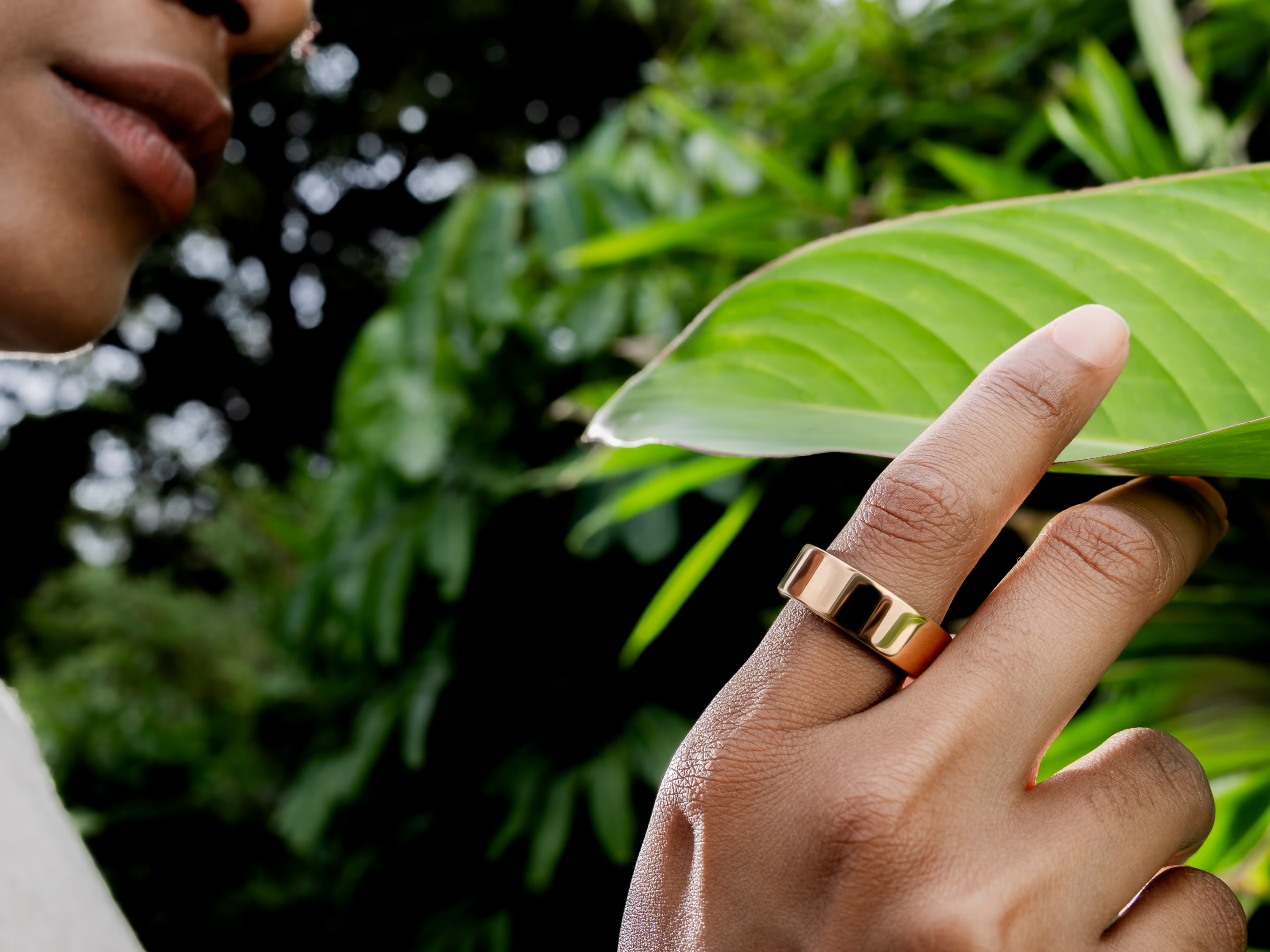 Main avec bague touche une grande feuille verte. Arrière-plan flou.