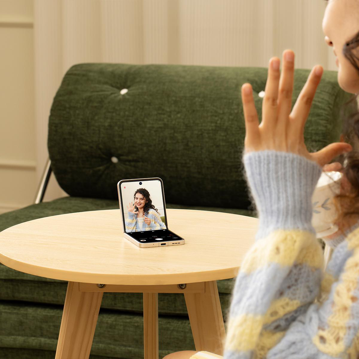 Eine Frau telefoniert per Video mit einer Person auf einem Klapphandy. Sie sitzt auf Couch.