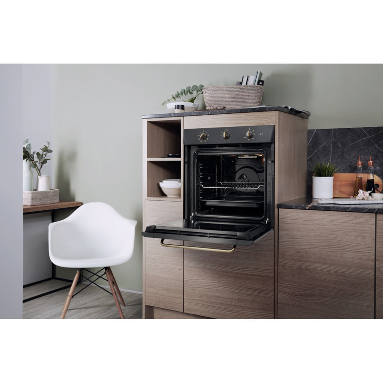 Un forno aperto in un mobile da cucina con piante e una sedia bianca nelle vicinanze.