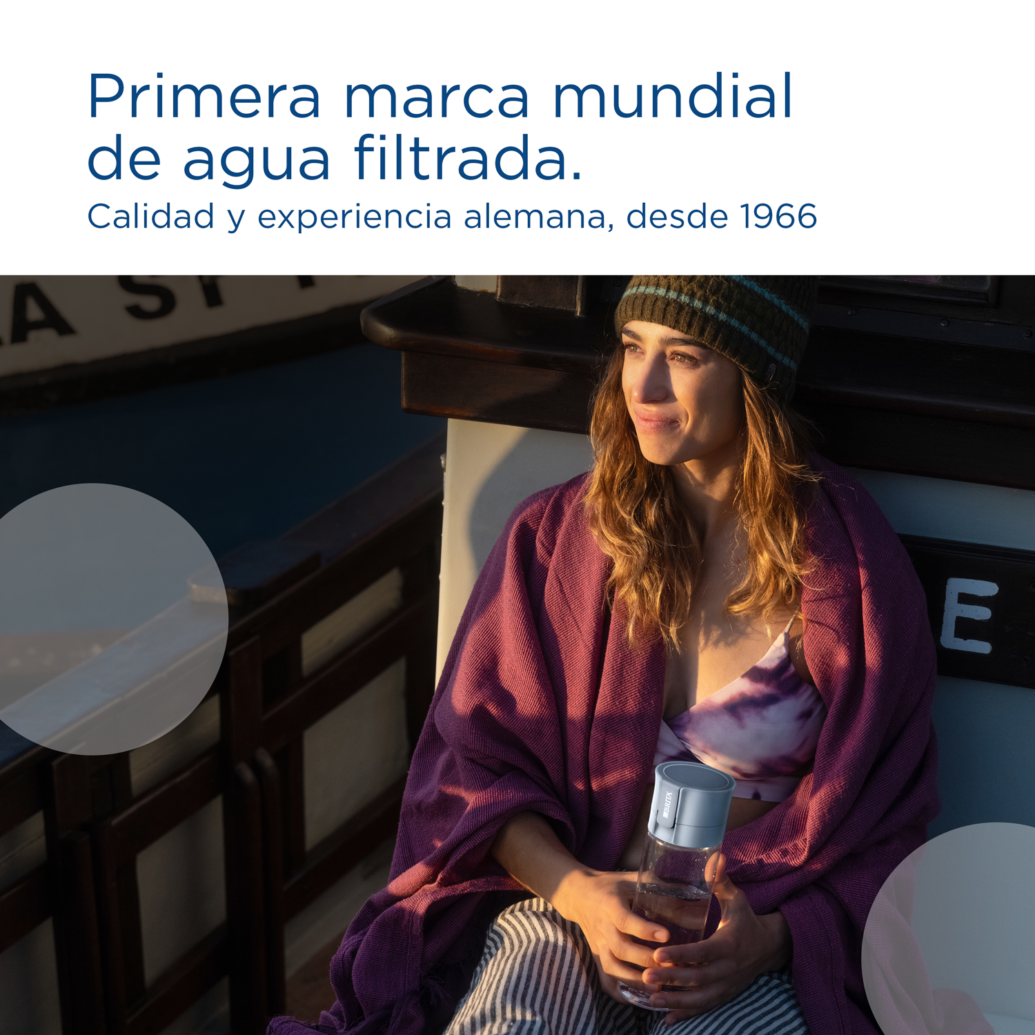 Una mujer sosteniendo una botella de agua, con texto sobre la marca y paisaje de fondo.