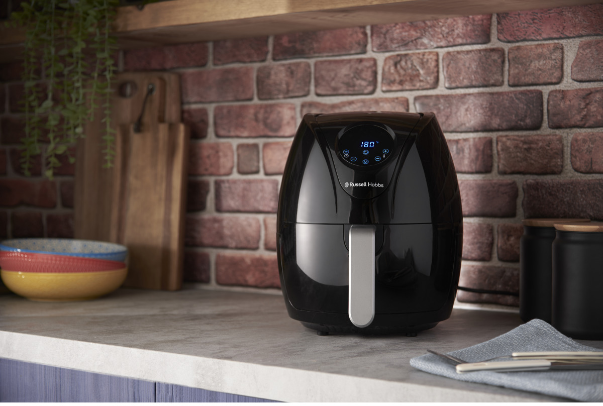 Friteuse à air noire Russell Hobbs sur un comptoir. En arrière-plan, un mur de briques et une planche à découper en bois.