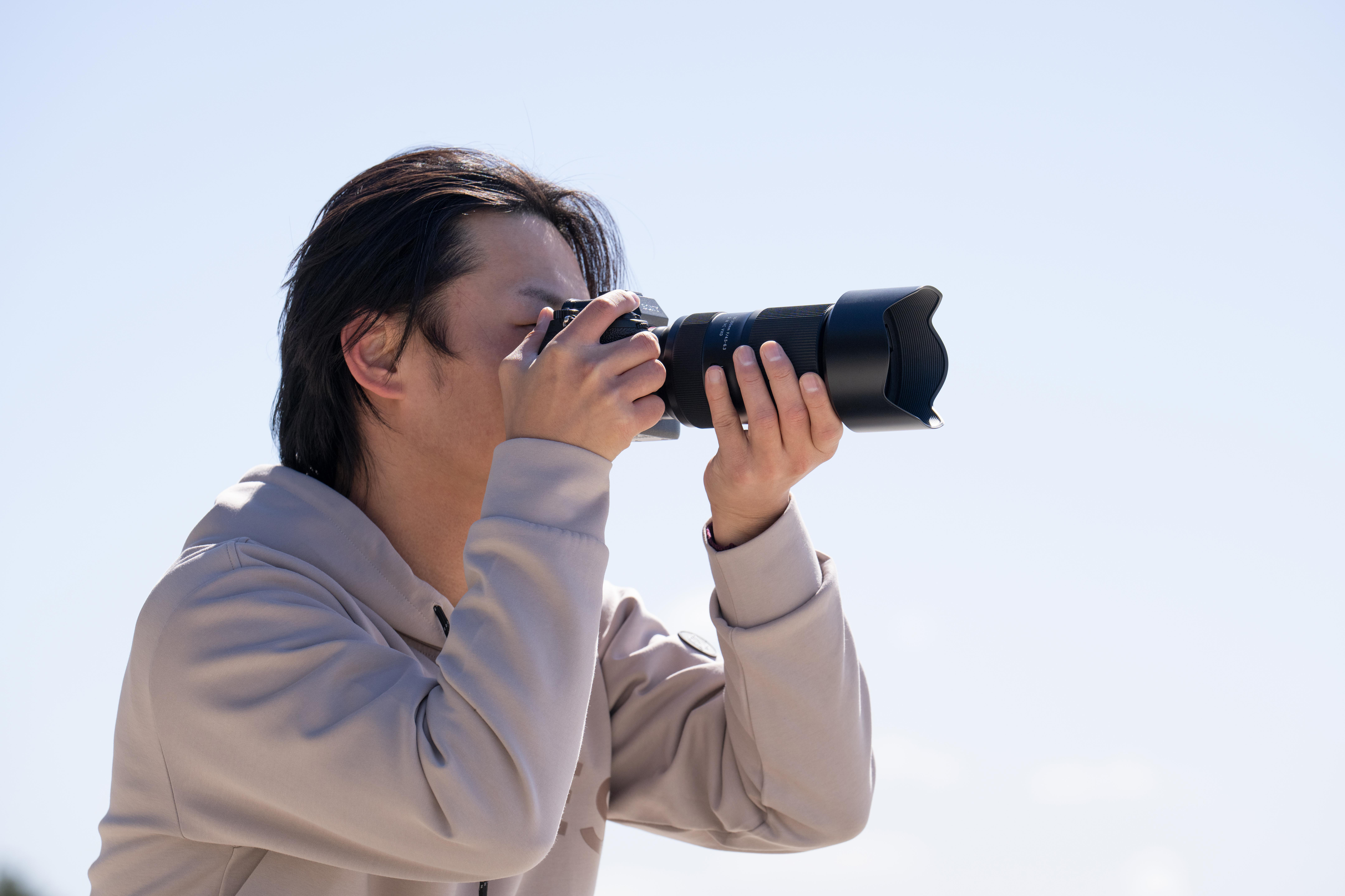 Ein Mann mit einer Kamera macht ein Foto vor einem klaren blauen Himmel.