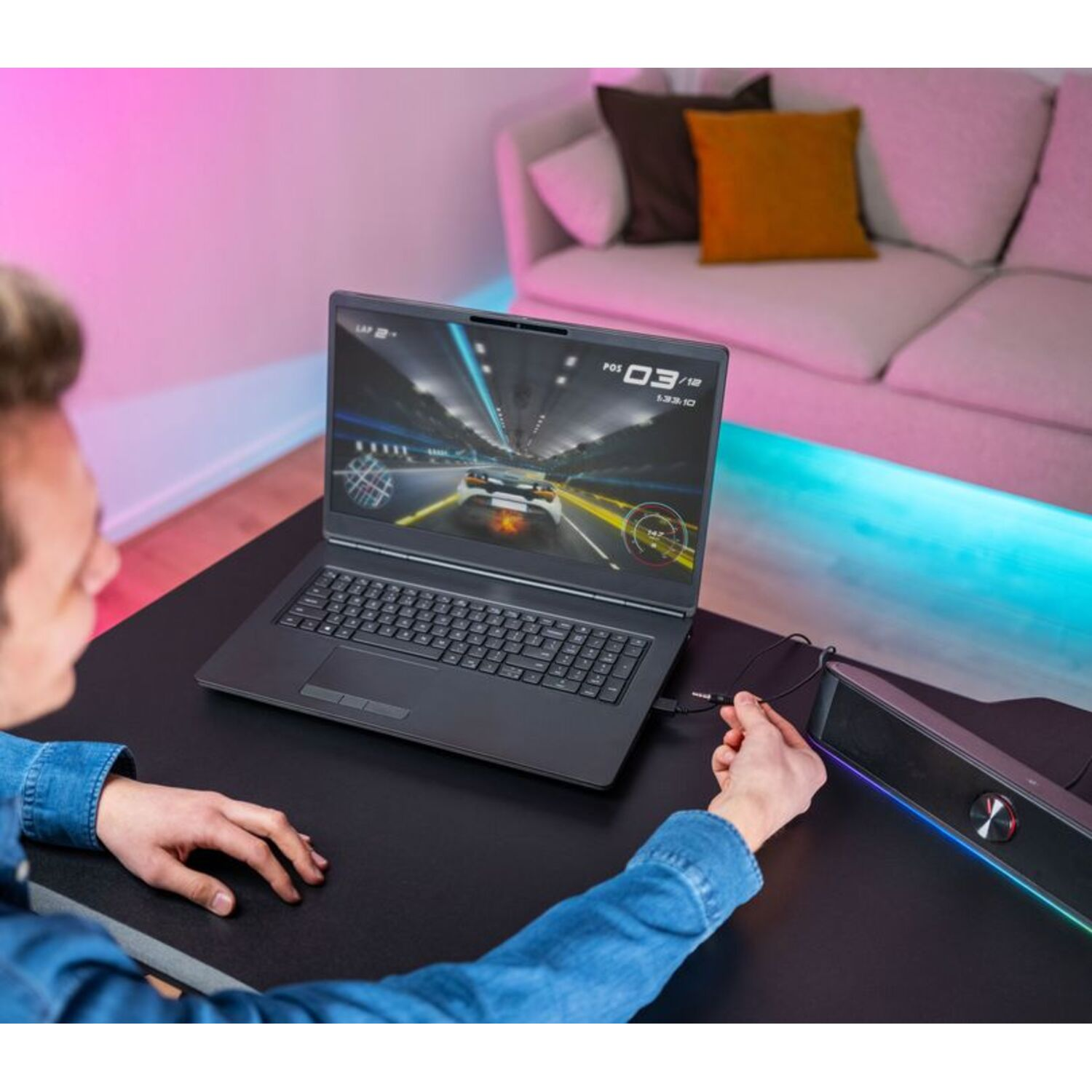 A person using a laptop with a racing game on the screen, connected to a speaker on a desk.