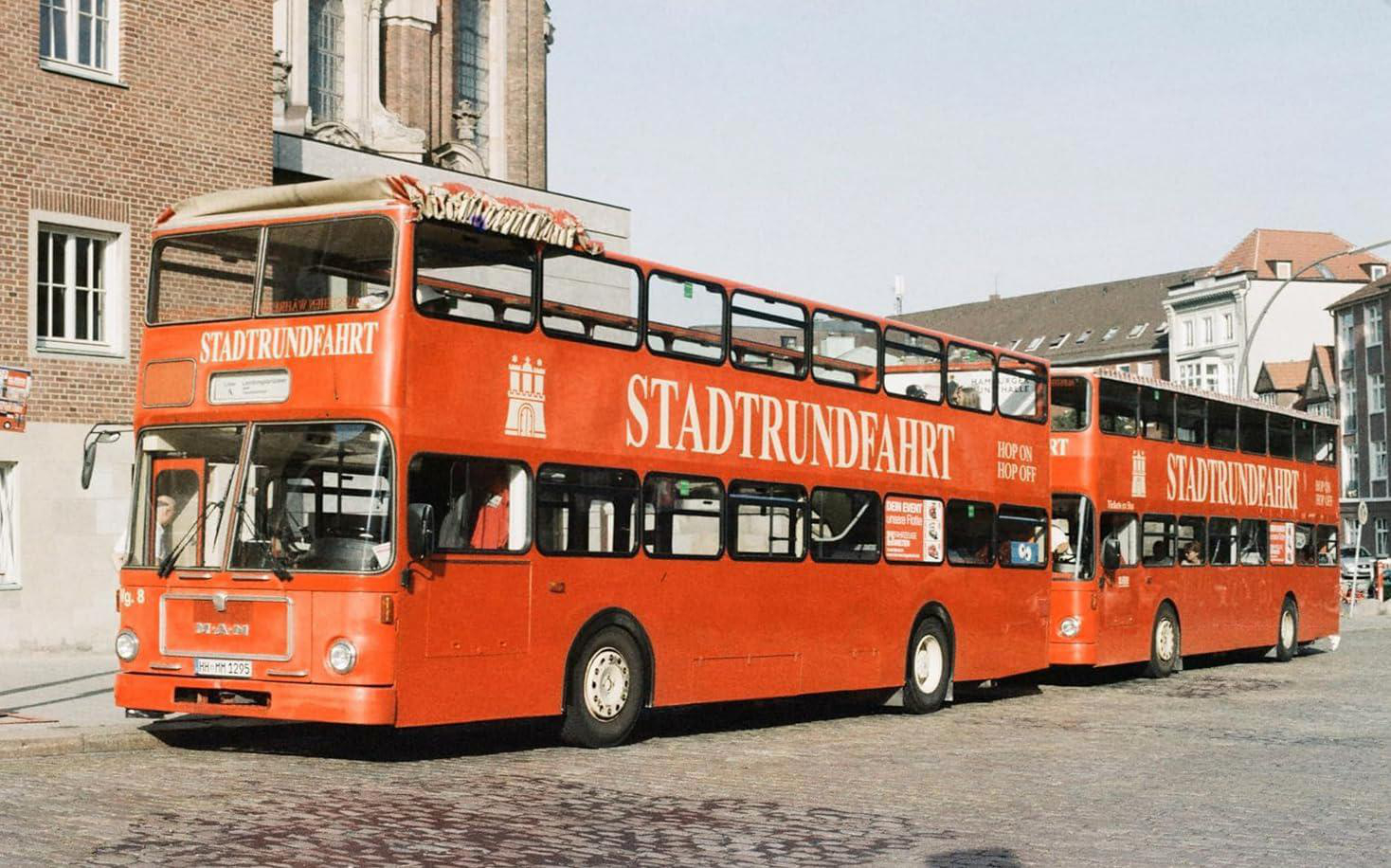 Zwei rote Doppeldeckerbusse mit Stadtrundfahrt-Beschriftung auf Straße.