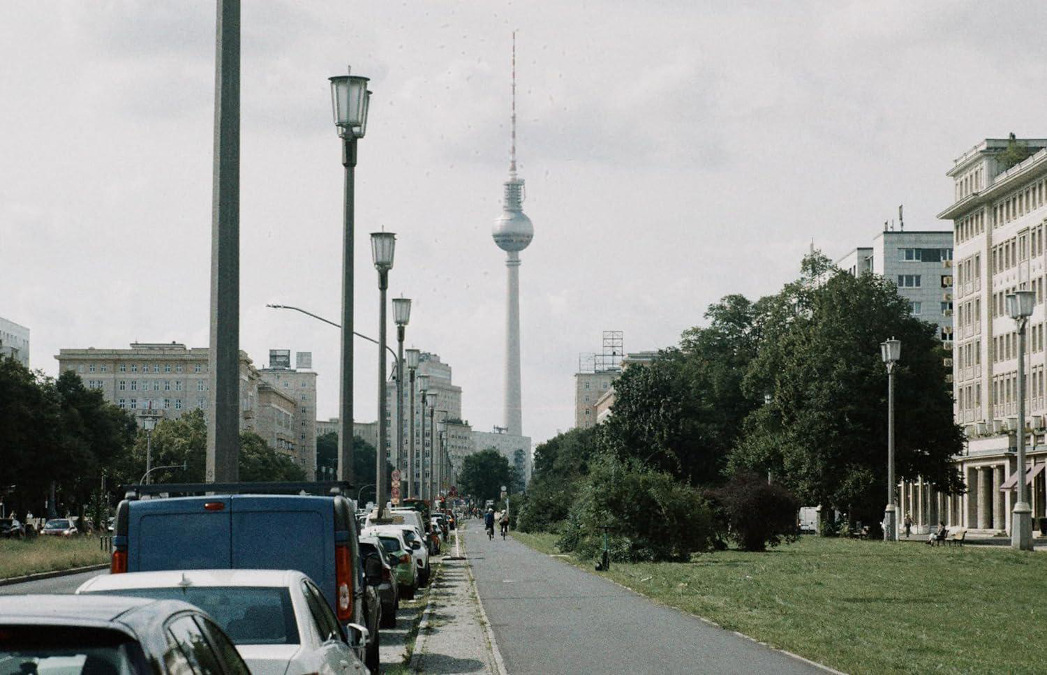 Eine Stadtstraßenszene mit Autos am Bürgersteig geparkt, ein hoher Turm im Hintergrund.