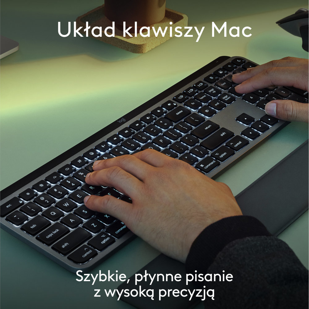 Dłonie piszące na czarnej klawiaturze, układ Mac, na zielonej powierzchni.