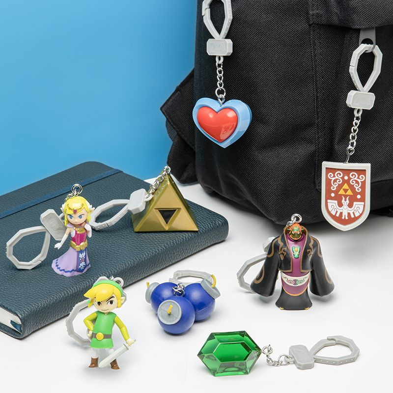 Varios llaveros de La Leyenda de Zelda cuelgan de una mochila y se apoyan en un cuaderno.