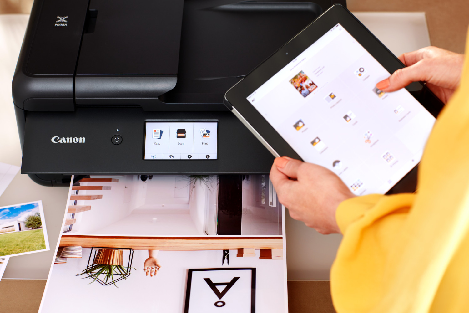 A woman holding a tablet, connected to a printer printing a photo.