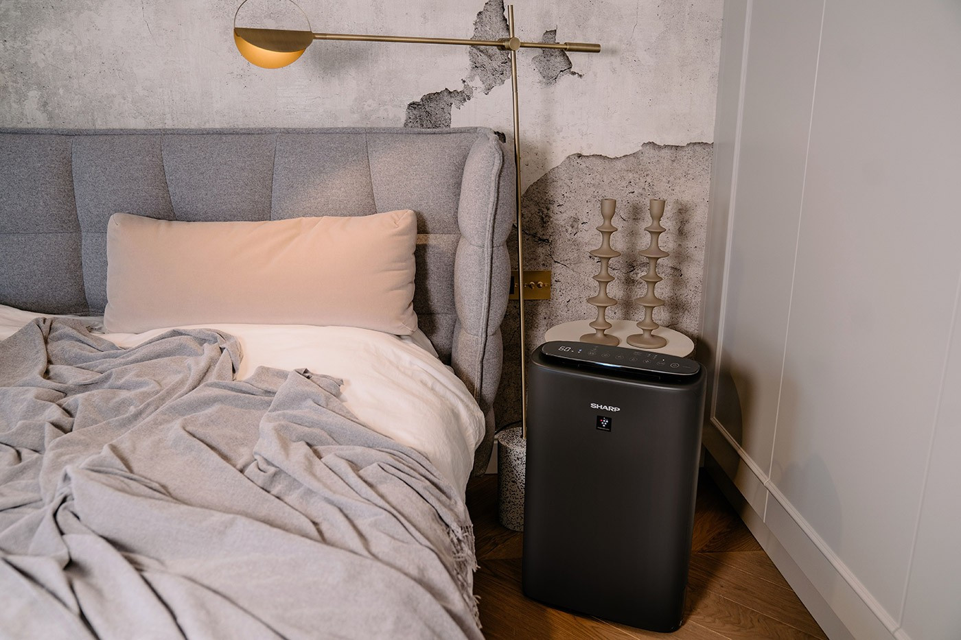 Scena w sypialni z łóżkiem, poduszką, oczyszczaczem powietrza i lampą. Stolik nocny ze świecami.