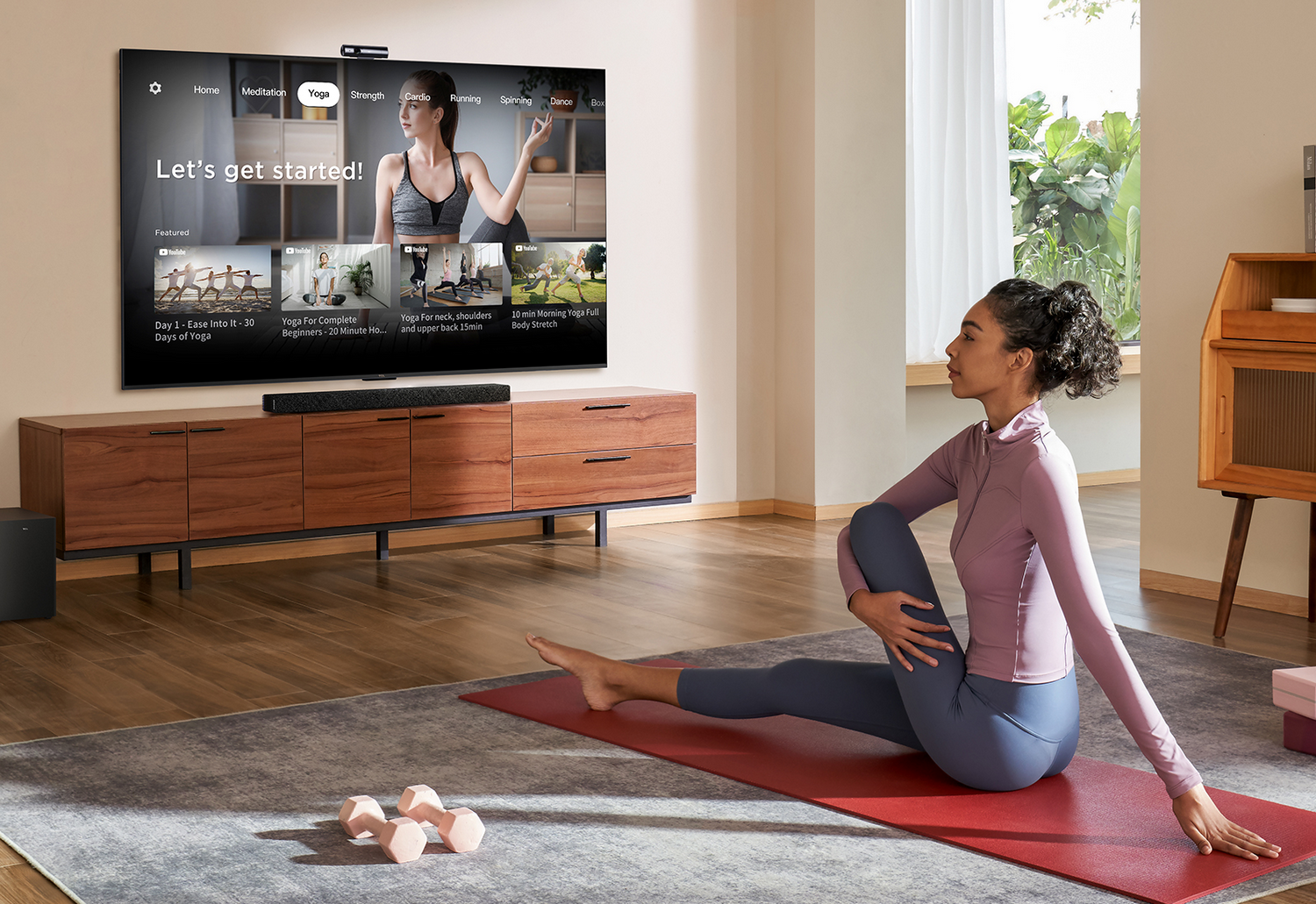 Mujer haciendo yoga en una sala de estar, viendo un tutorial de yoga en un televisor grande.