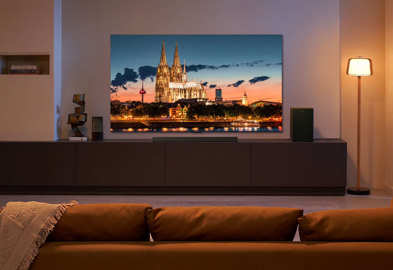 Escena de sala de estar con TV grande. Paisaje urbano en la pantalla. Sofá, lámpara y otros muebles.
