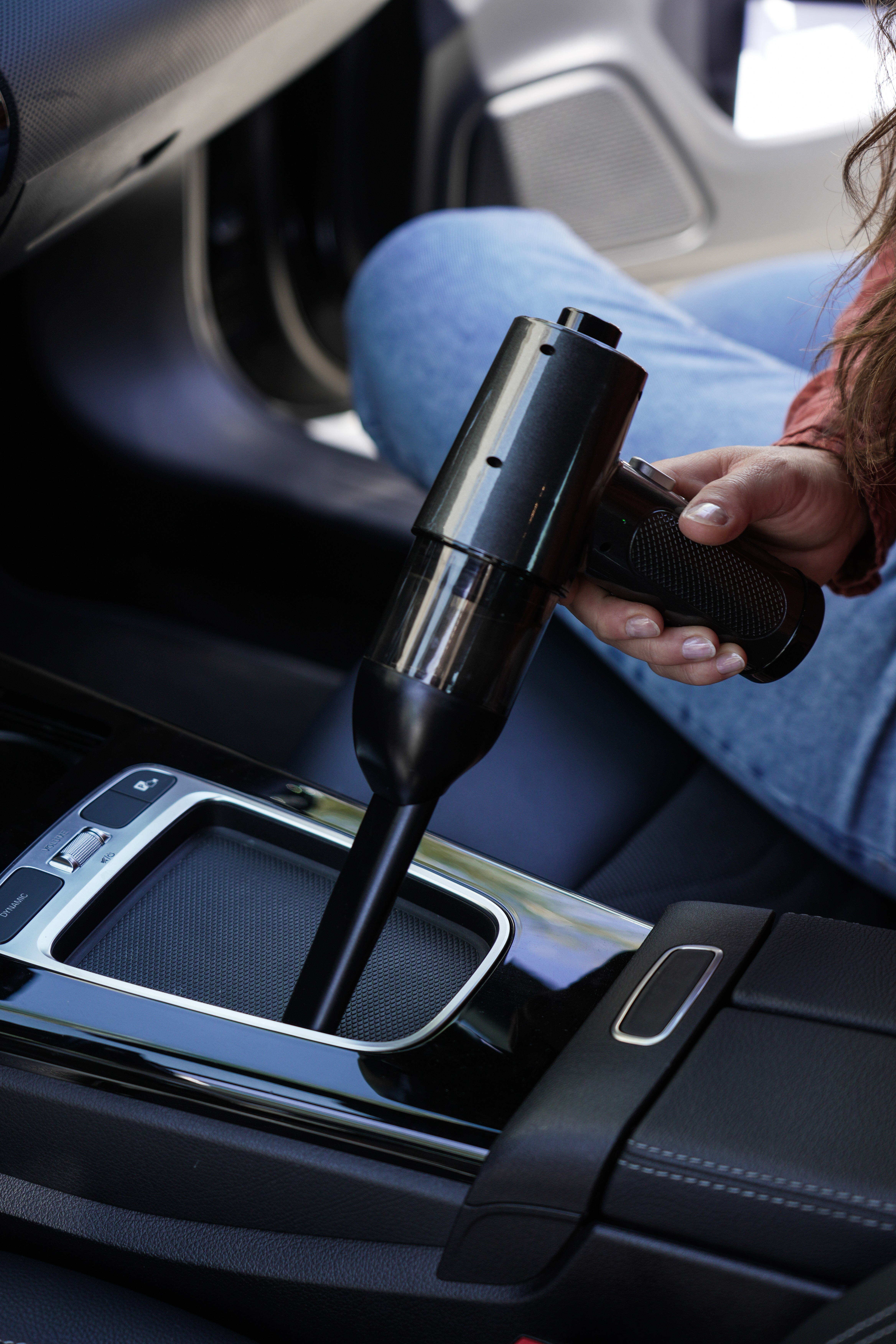 Eine Person hält einen schwarzen Handstaubsauger in einem Auto. Fokus auf Innenraum und Gerät.