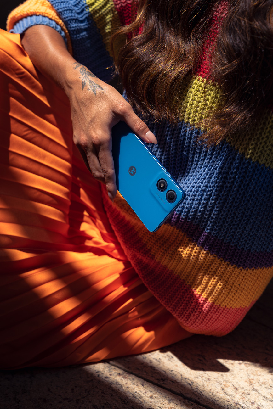 Osoba trzyma niebieski smartfon, nosząc pasiasty sweter i pomarańczową spódnicę.