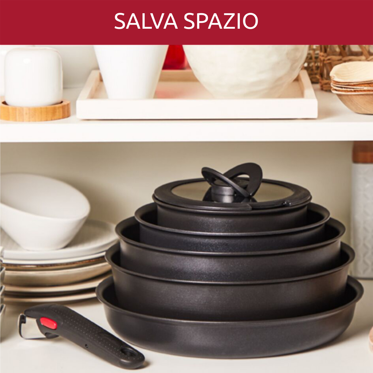 Pila di padelle nere con coperchio, mensola con oggetti bianchi e manico rosso.
