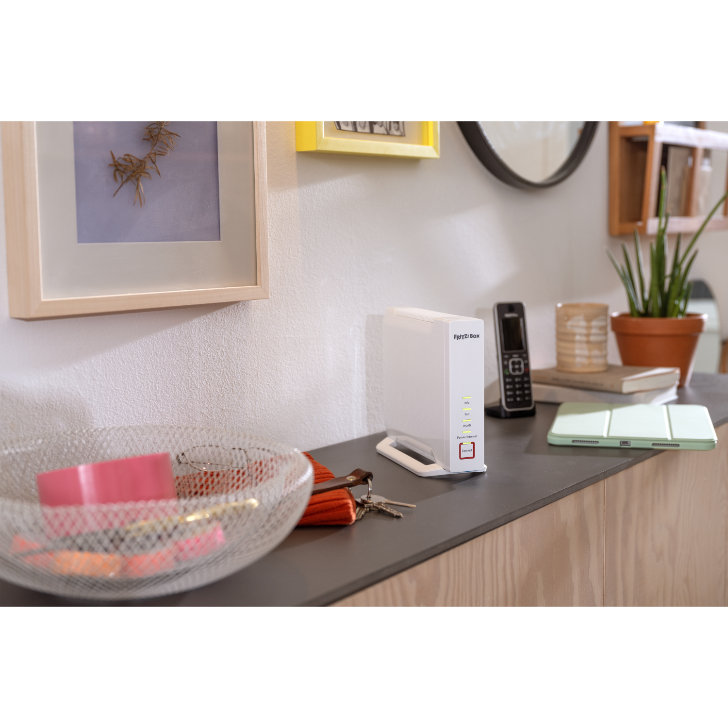 A white router and phone on a gray counter. There is a framed picture and a small decorative bowl.